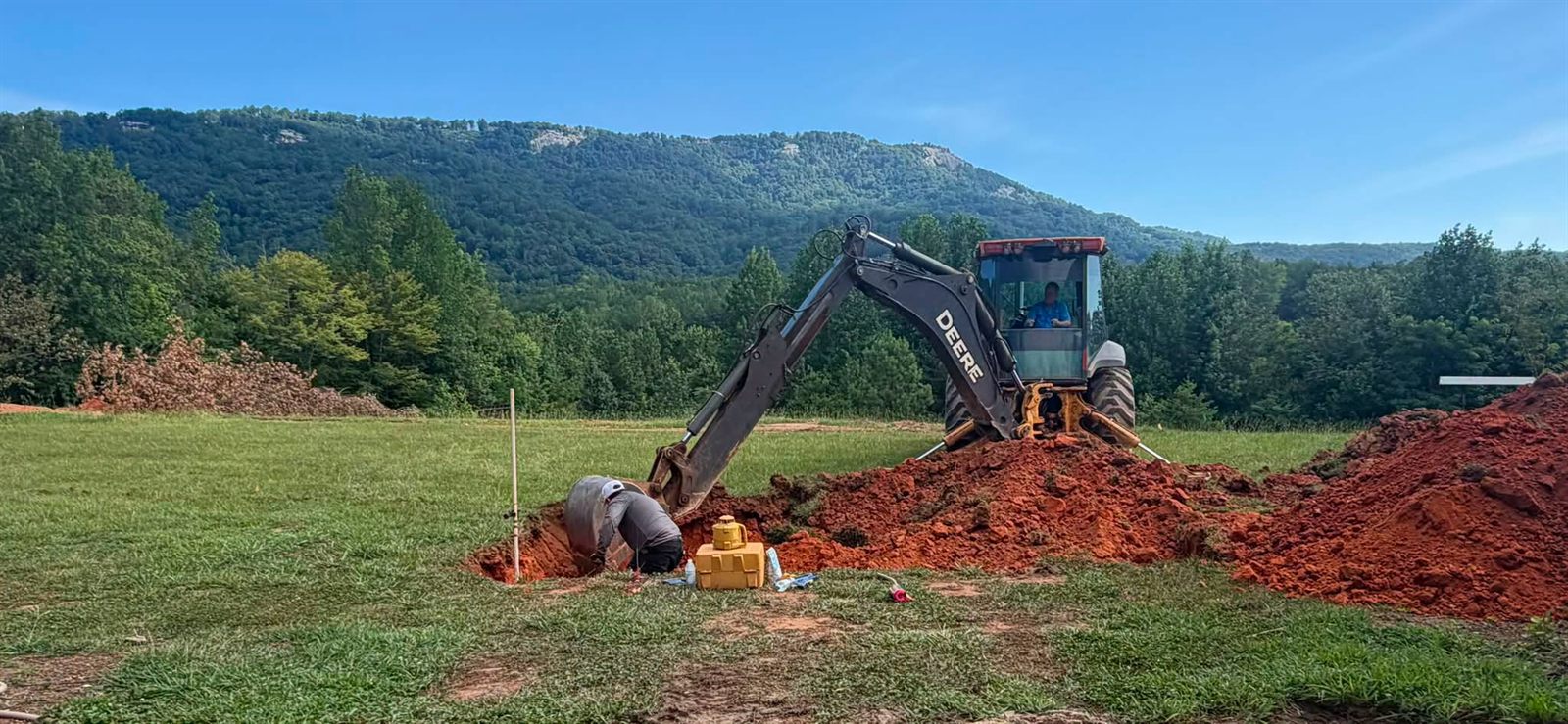 Backhoe digging plumbing trenches on a pool site with a mountain ridge in the background