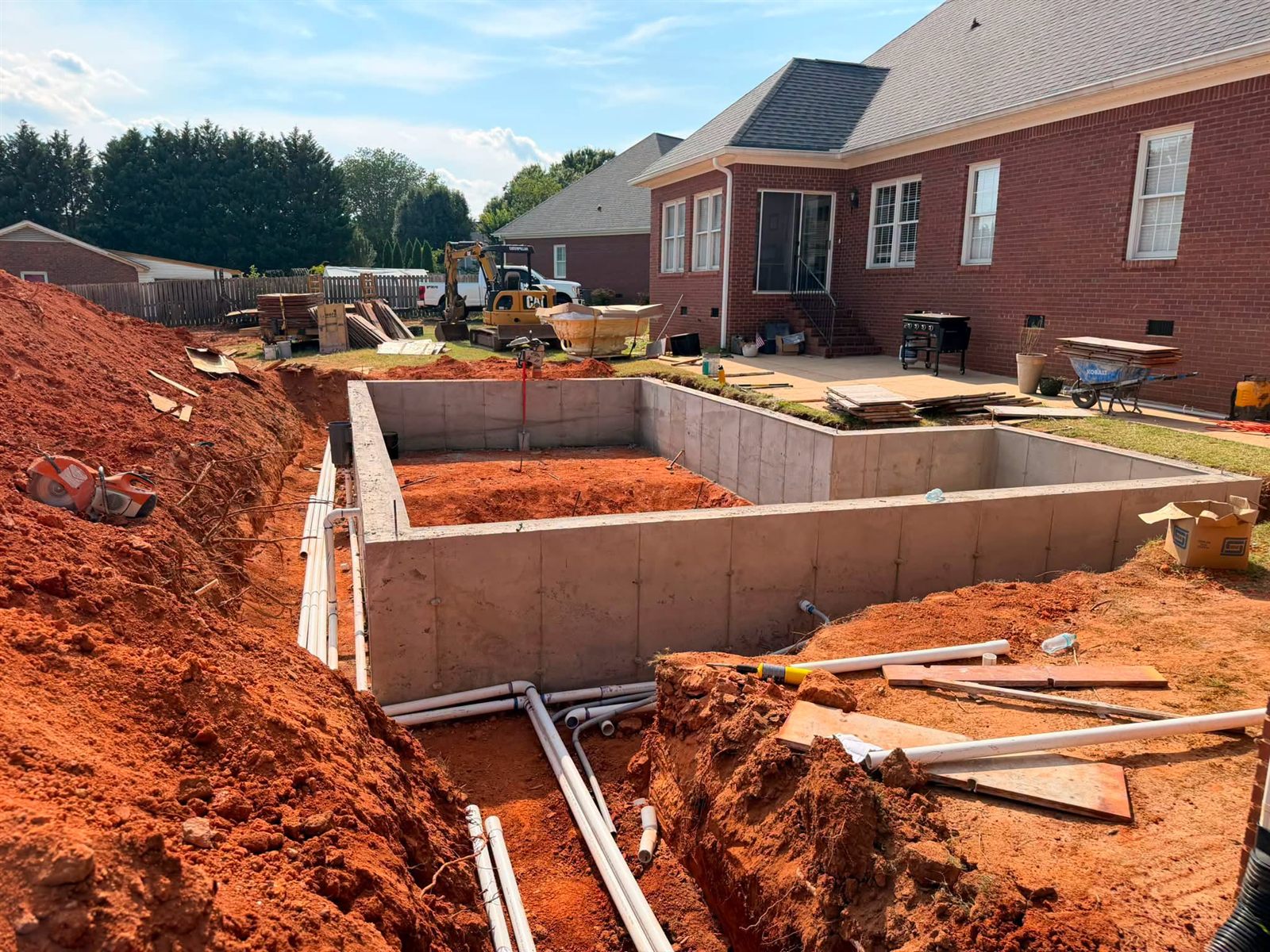 Poured concrete pool walls with plumbing runs trenched in beside a brick home
