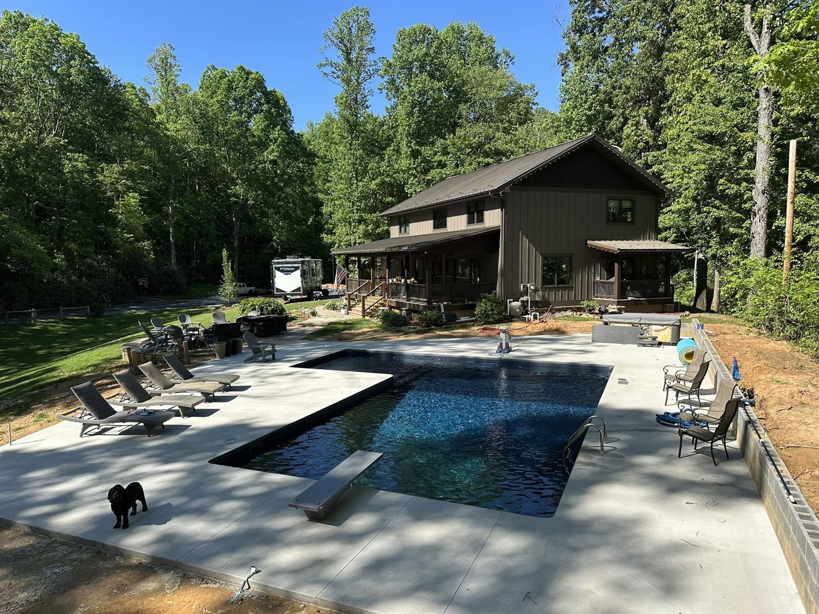 Large rectangular pool with a diving board and dark liner behind a board-and-batten home