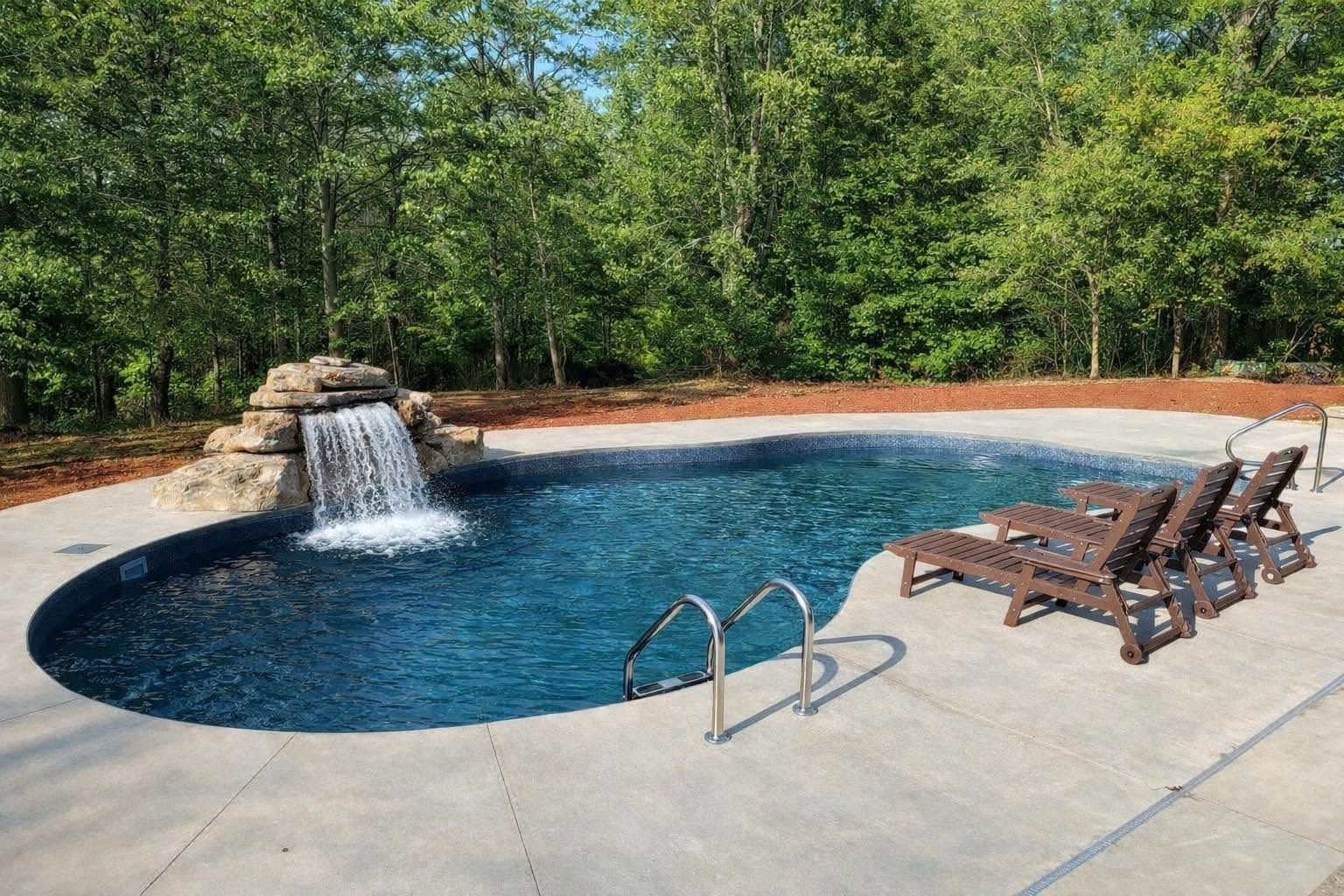Freeform pool with a natural stone waterfall and loungers on a broad concrete deck
