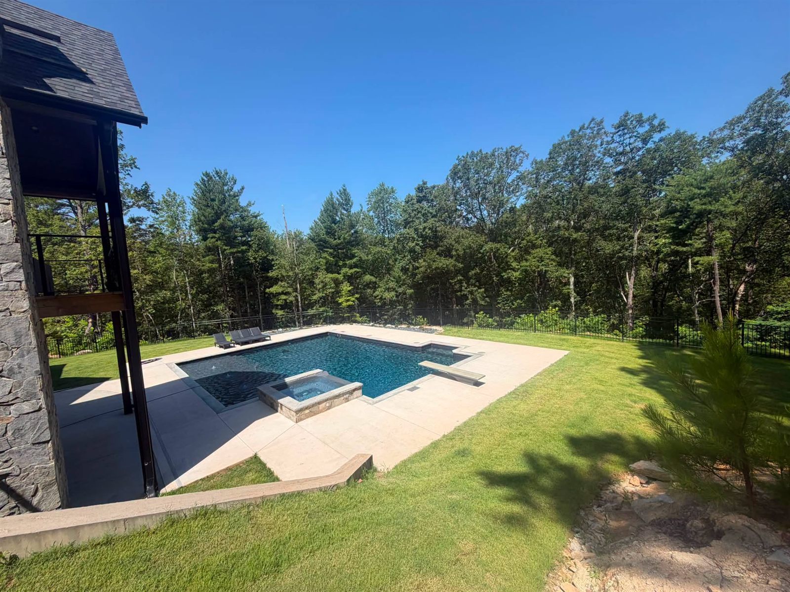 In-ground pool with a raised spa and diving board behind a stone home on a wooded hillside